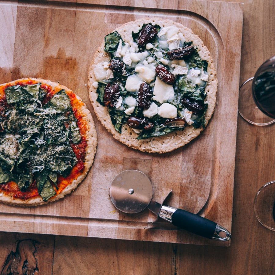 Twee pizzas op een houten plank met een pizzasnijder