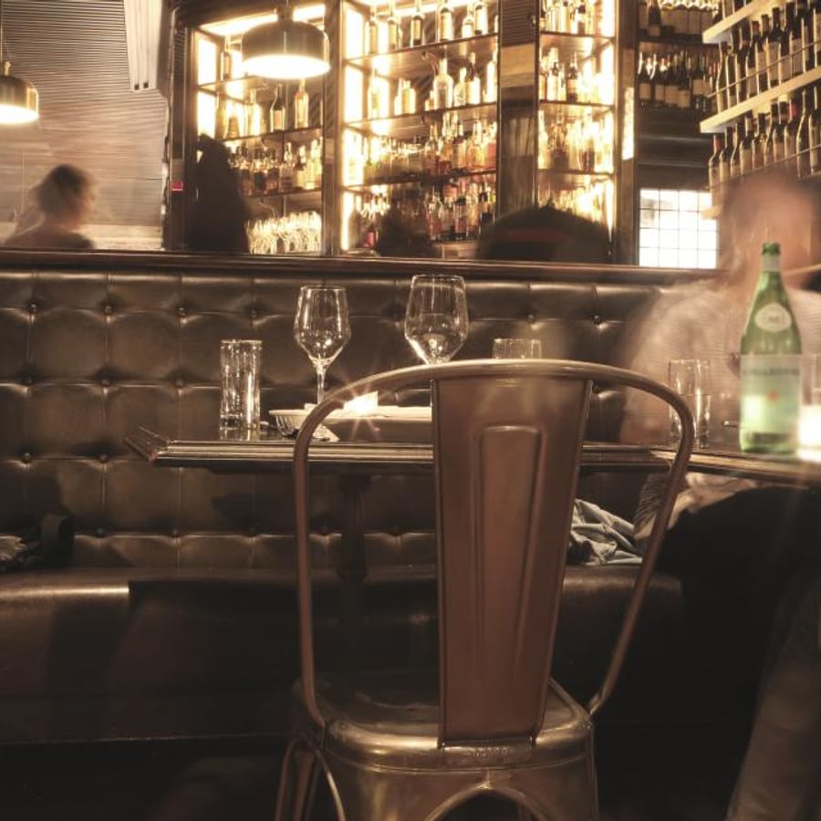 Zitgedeelte van een bistro met leren bank en een verlichte bar