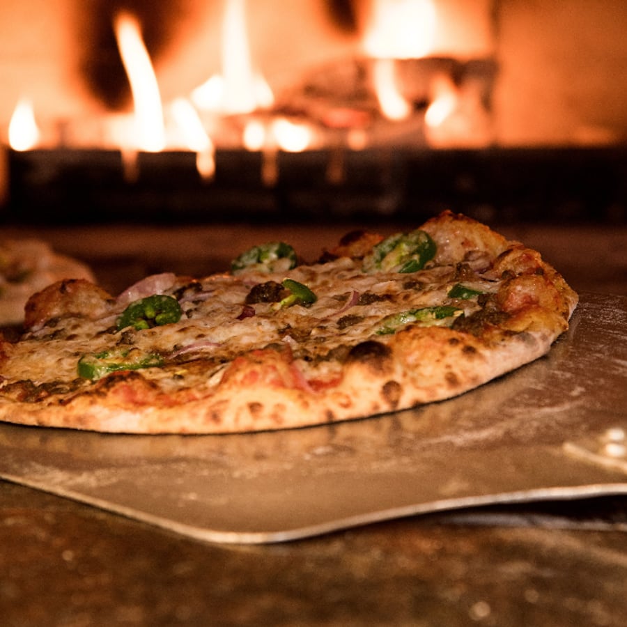 Pizza op een schep voor de brandende houtoven