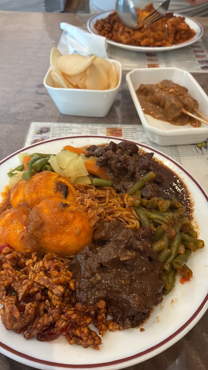 Bord rames met telur balado, rendang, bami, sperziebonen en sambal goreng tempe, met kroepoek en sate in pindasaus.